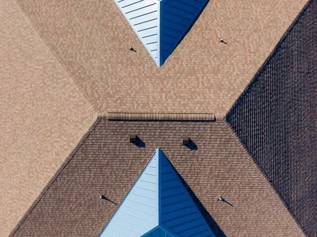 Overhead view of a brown shingle roof with a ridge vent and several small roof vents