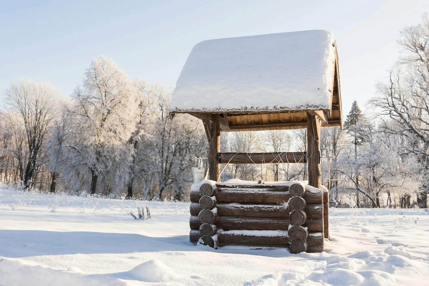 Wooden well with a snow-covered gable roof in a frosty, sunlit winter field