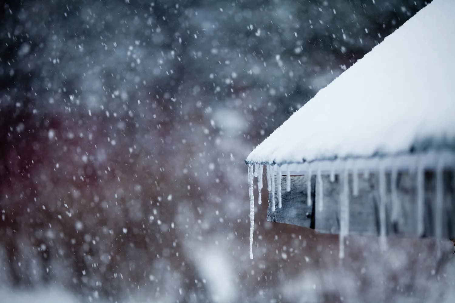 Icicles hanging from a snow-covered roof edge during a heavy snowfall