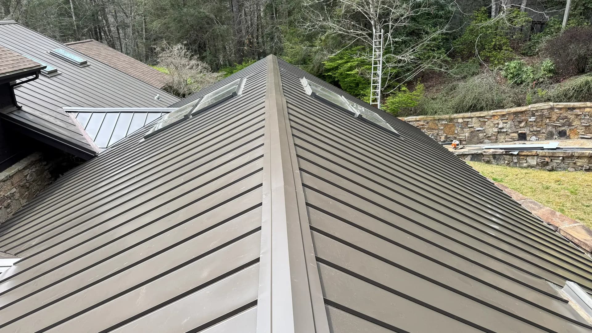 Bronze standing seam metal hip roof with skylights, installed by True North Roofing on a wooded mountain property