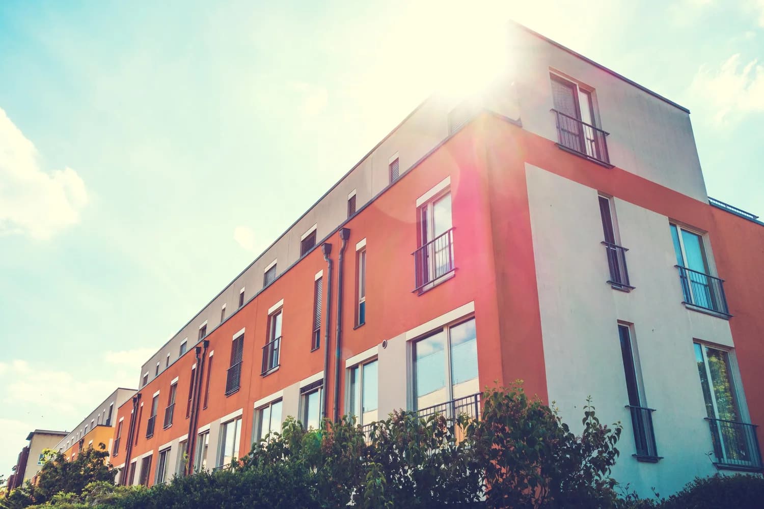 Orange and white flat-roofed townhouse block seen from below in bright sunlight