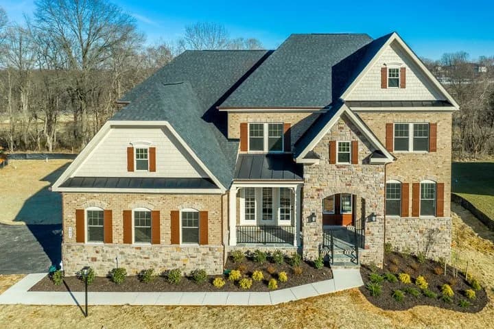 Two-story brick and stone house with a dark gray shingle roof and red shutters