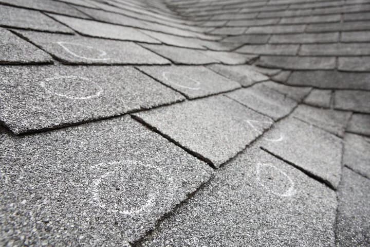 Gray asphalt shingles with chalk circles marking spots found during an inspection