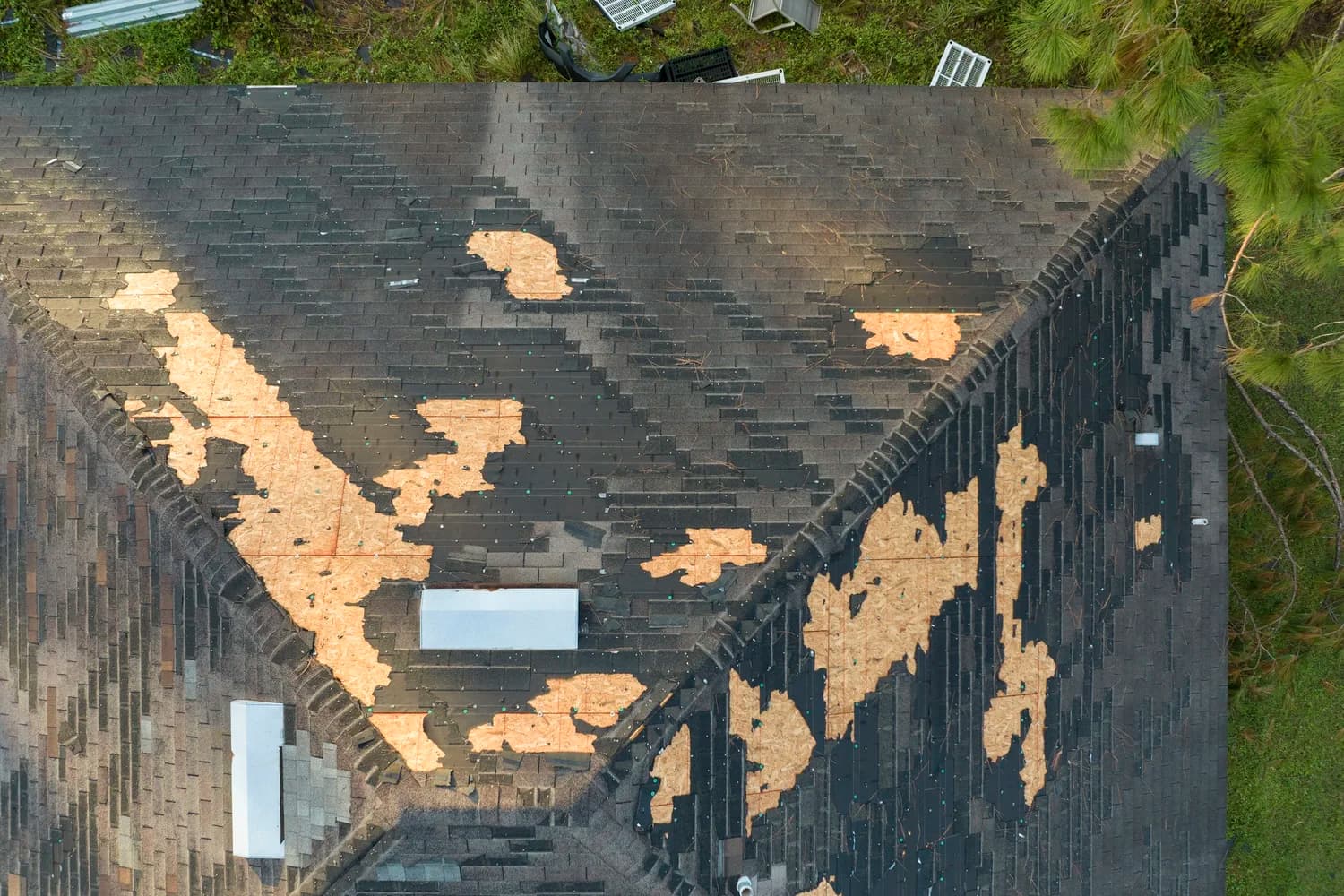 Aerial view of a storm-damaged shingle roof with patches of bare plywood decking showing